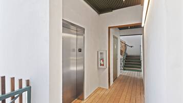 Un couloir doté d’un plancher en bois, d’un ascenseur en métal et d’un escalier menant à un autre niveau.