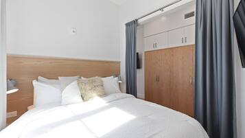Une chambre à coucher moderne avec une tête de lit en bois, un grand lit avec une literie blanche, une table de chevet avec une lampe et une armoire avec un miroir.
