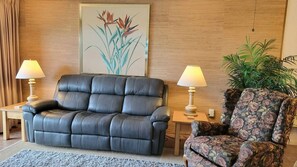 A living room with a leather sofa, two side tables with lamps, a floral armchair, and a large framed botanical print on the wall. - 108 - 2 BR Poolside Great View (New Smyrna Beach)