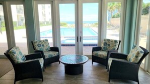 A room with four wicker chairs with floral cushions, a round coffee table, and large glass doors leading to a pool area. - 108 - 2 BR Poolside Great View (New Smyrna Beach)