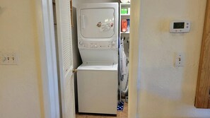 A laundry area with a washer and dryer, a thermostat, and a door leading to a room. - 108 - 2 BR Poolside Great View (New Smyrna Beach)