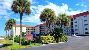A hotel with multiple floors and a red roof, surrounded by palm trees and a parking lot. - 108 - 2 BR Poolside Great View (New Smyrna Beach)