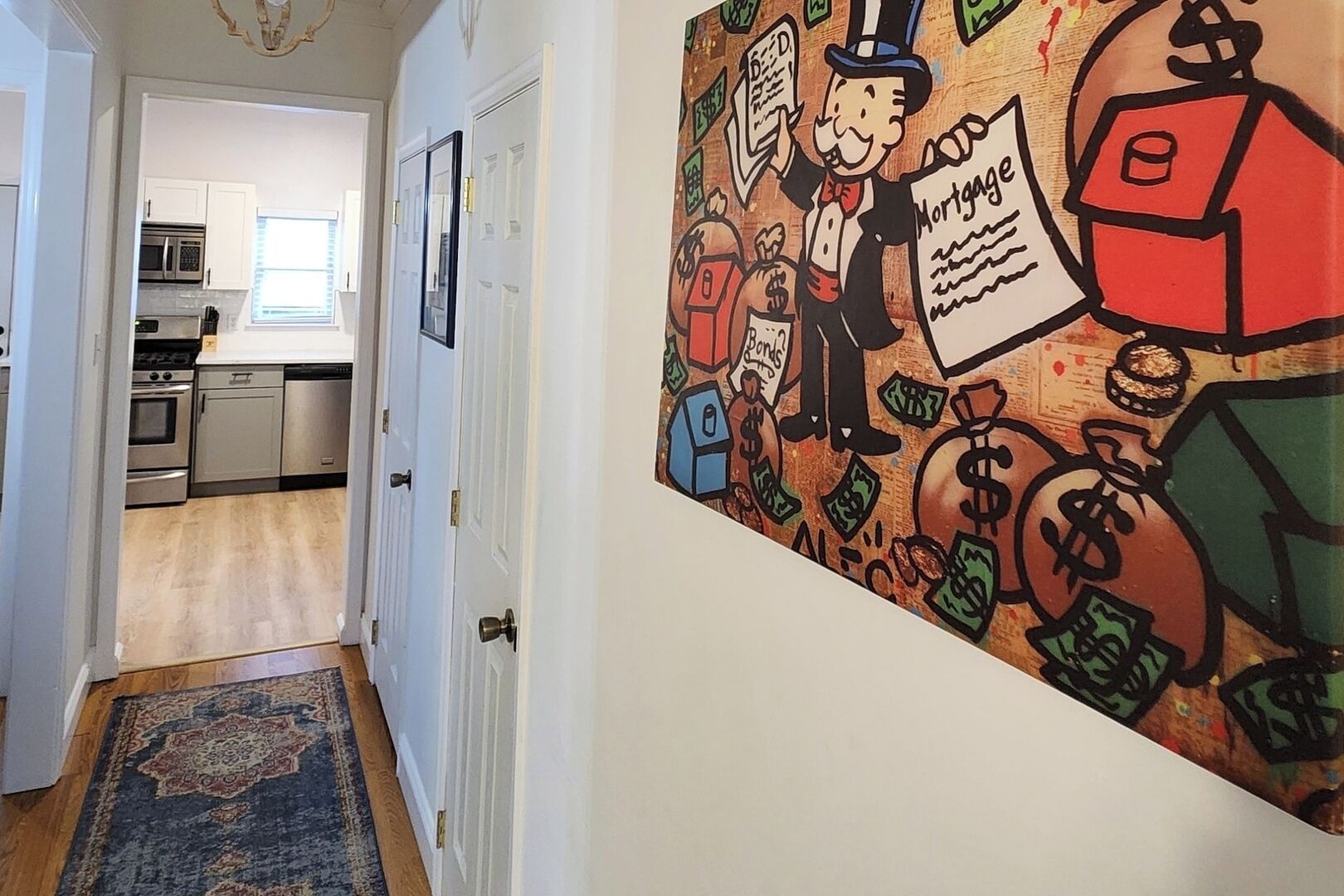 Un couloir avec une cuisine visible au fond, un tapis à motifs et une fresque murale représentant un personnage de dessin animé tenant un document hypothécaire.