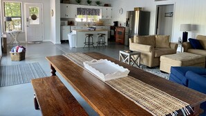 Ein geräumiger Wohnbereich mit einer hölzernen Bank, einem Sofa und einem Couchtisch. Im Hintergrund ist eine Küche mit weißen Schränken und einem Kühlschrank erkennbar.