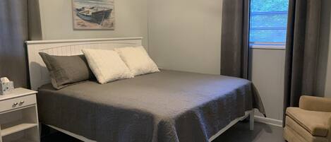 A bedroom with a bed, a nightstand, a chair, and a window with curtains.
