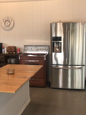A kitchen with a stainless steel refrigerator, a vintage stove, wooden cabinets, and a clock on the wall.