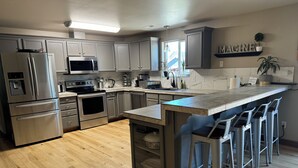 A modern kitchen with stainless steel appliances, a wooden floor, and a bar area with stools. - Group Fun - 7 Separated Sleeping Areas! (Redmond)