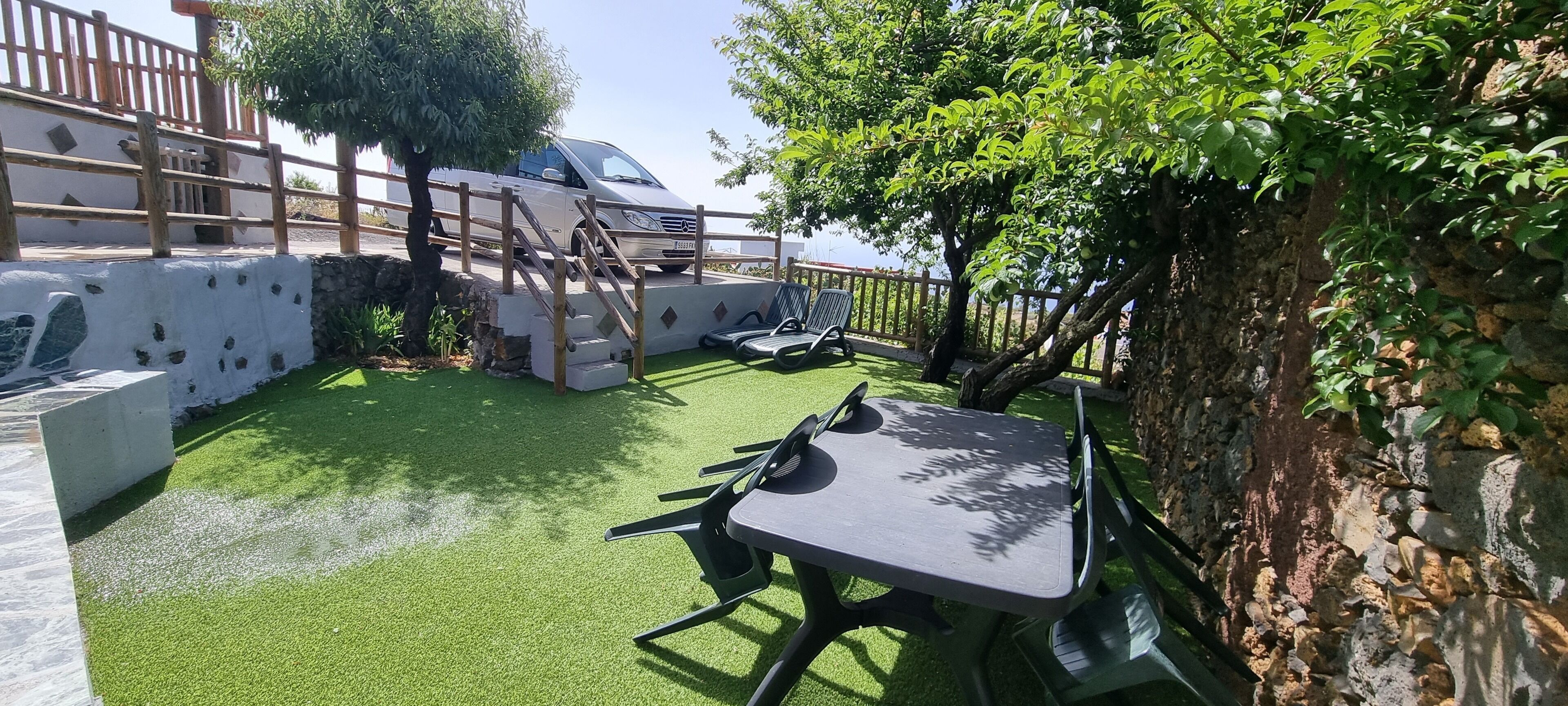 A patio with artificial grass, a table, chairs, and a car parked nearby.