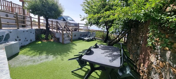 A patio with artificial grass, a table, chairs, and a car parked nearby.