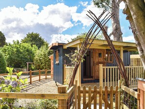 Een rustieke houten chalet met een houten terras en een omheinde tuin.
