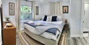 Ein ordentlich eingerichtetes Schlafzimmer mit einem Bett, Nachttischen, einem Fenster und Blick auf Grünfläche.