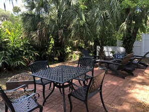 Eine Terrasse mit einem Metalltisch und -stühlen, umgeben von üppiger Bepflanzung und einem weißen Zaun.