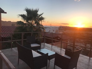 A terrace with wicker furniture and a view of the sunset over a cityscape. - loft verde (puerto peñasco)