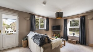 Ein gemütliches Wohnzimmer mit einer Couch, einem Flachbildfernseher und einem großen Fenster mit Vorhängen.