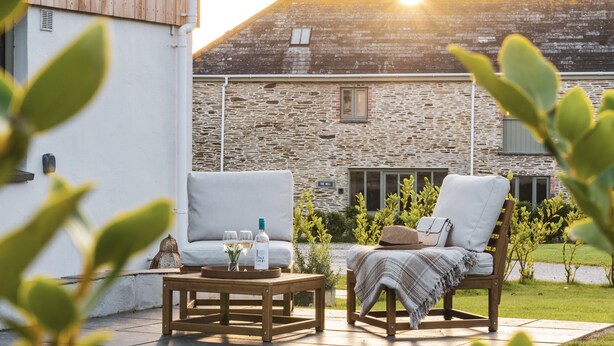 Eine Terrasse mit zwei weißen Korbstühlen, einem Holztisch und einer Weinflasche.