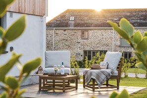 A patio with two white cushioned chairs, a wooden table, and a bottle of wine. - The Nooke at Bogee Farm - sleeps 2 guests  in 1 bedroom (Wadebridge)