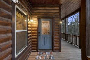 A wooden cabin entrance with a door, a welcome mat, and a porch with a railing.
