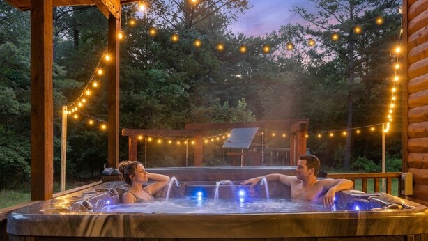 Een bubbelbad met twee personen die ontspannen, omringd door lichtjes en een houten terras.