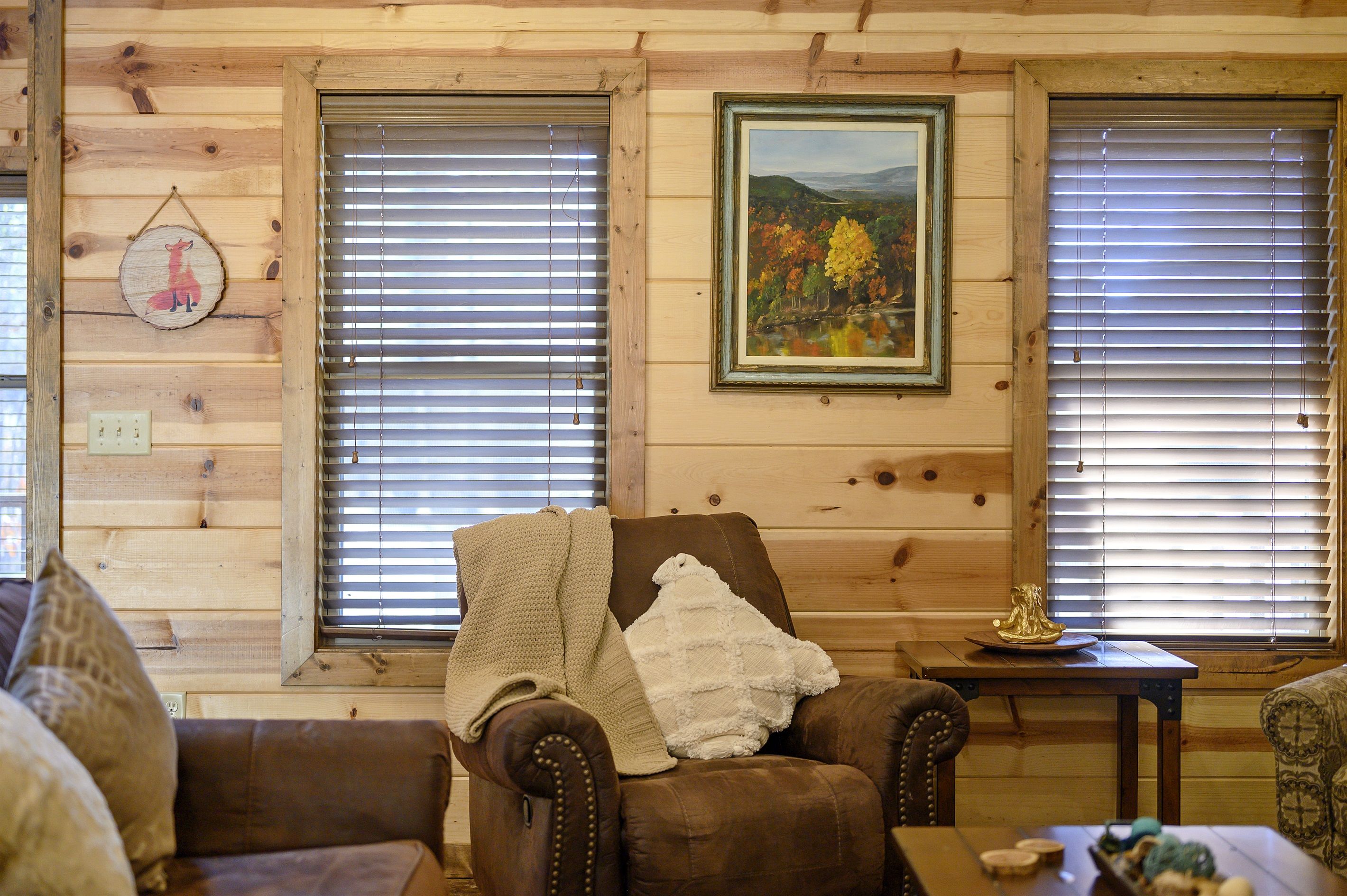 A cozy cabin interior with a brown leather armchair, a small table with a decorative item, and a framed painting on the wall.