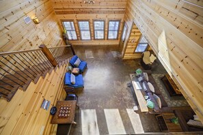 A wooden cabin interior with a staircase leading to a loft area, a sofa set, a dining table, and a fireplace.