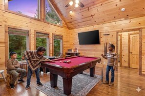 A wooden interior with a pool table, a television, and large windows.