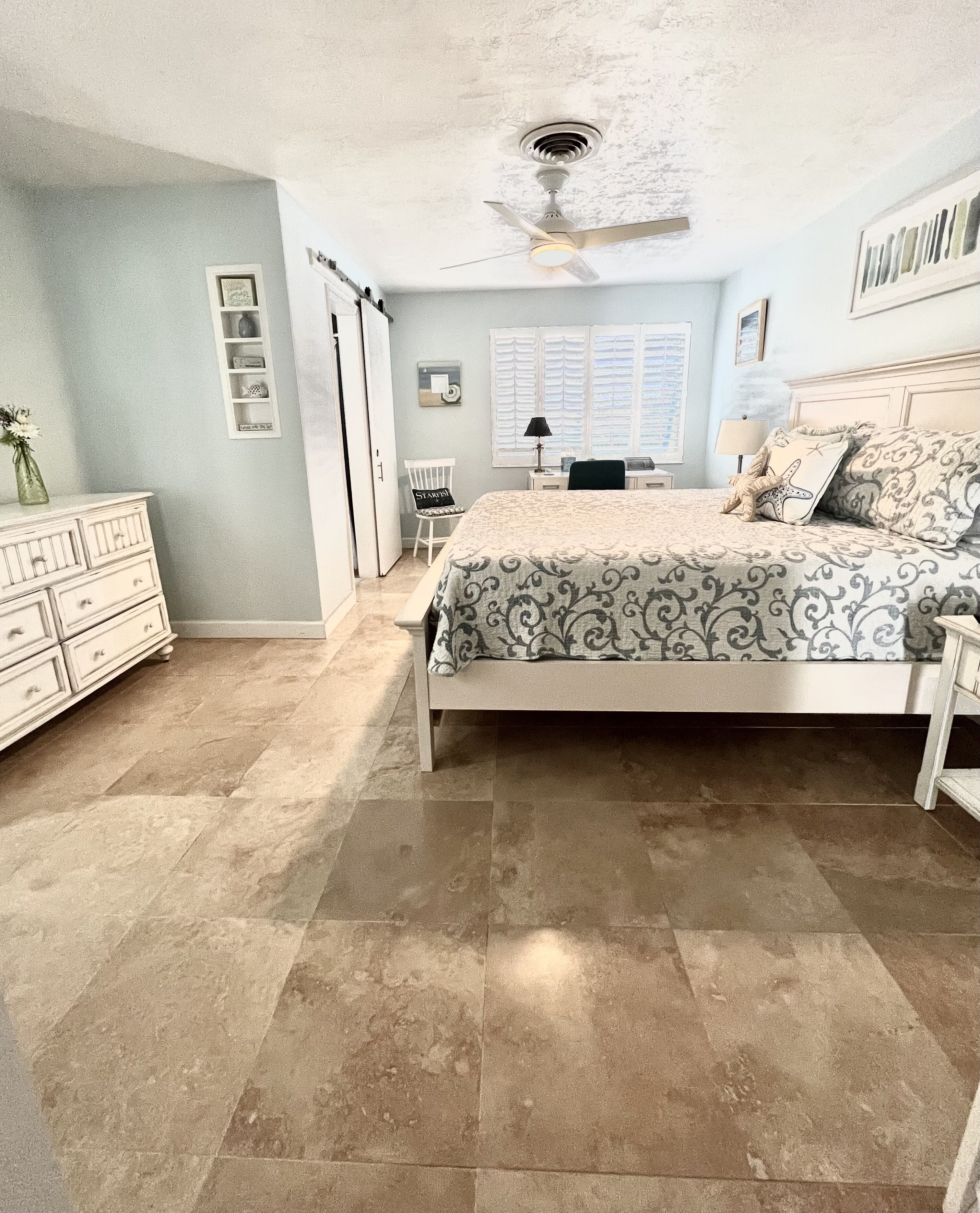 A bedroom with a bed, dresser, chair, and a ceiling fan.