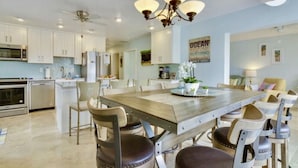 A modern kitchen with white cabinets, a wooden dining table, and a chandelier.