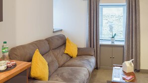 A cozy living room with a brown sofa, two yellow cushions, a wooden side table with a bottle, jars, and a tissue box. - 1 bedroom accommodation in Girvan (Girvan)