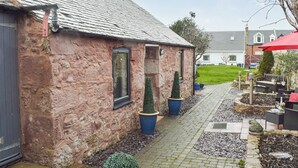 A stone building with a tiled roof, a paved pathway, and potted plants. - 1 bedroom accommodation in Girvan (Girvan)