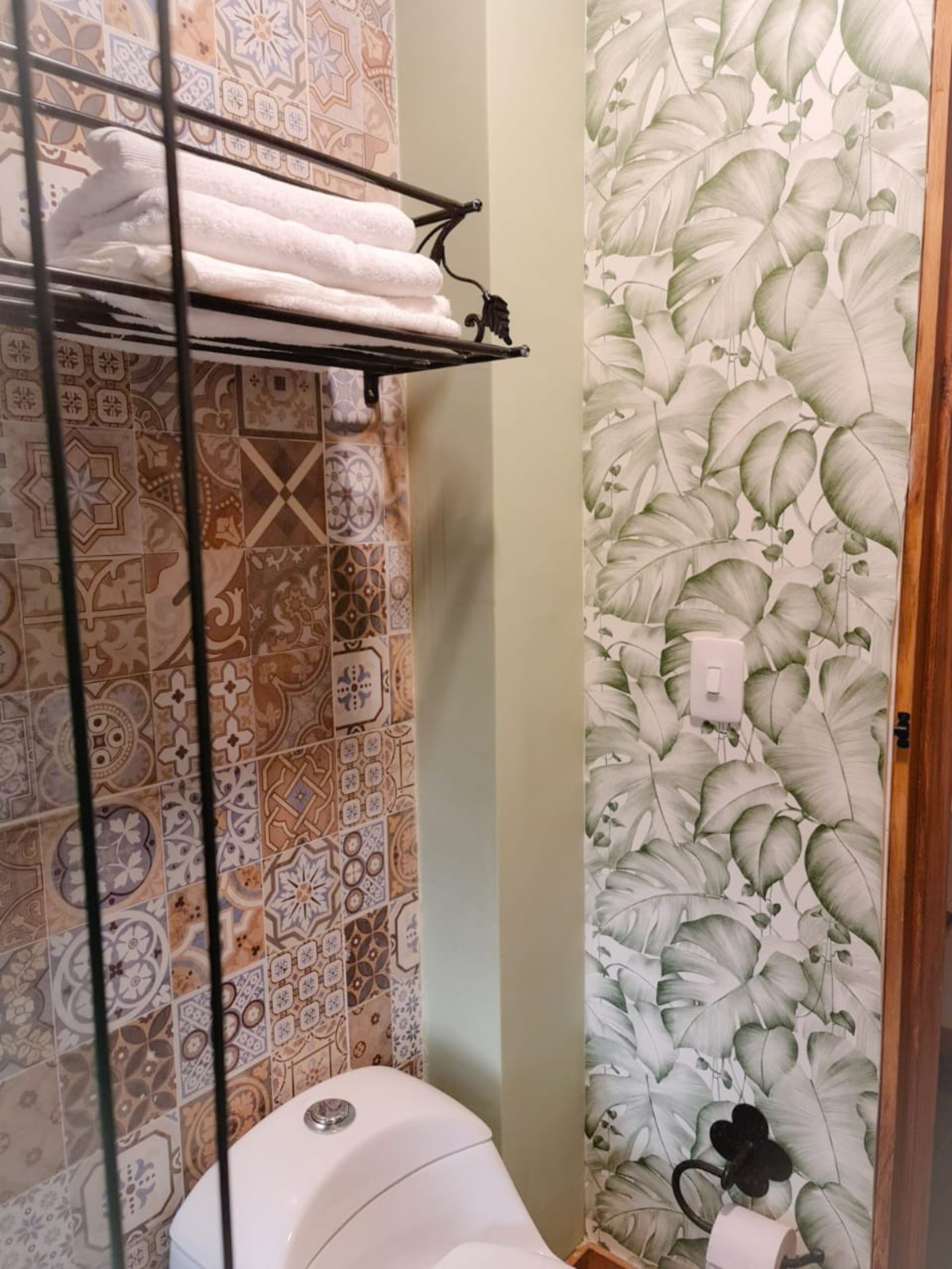Un baño con baldosas estampadas, inodoro, toallero y cortina de ducha con diseño de hojas.