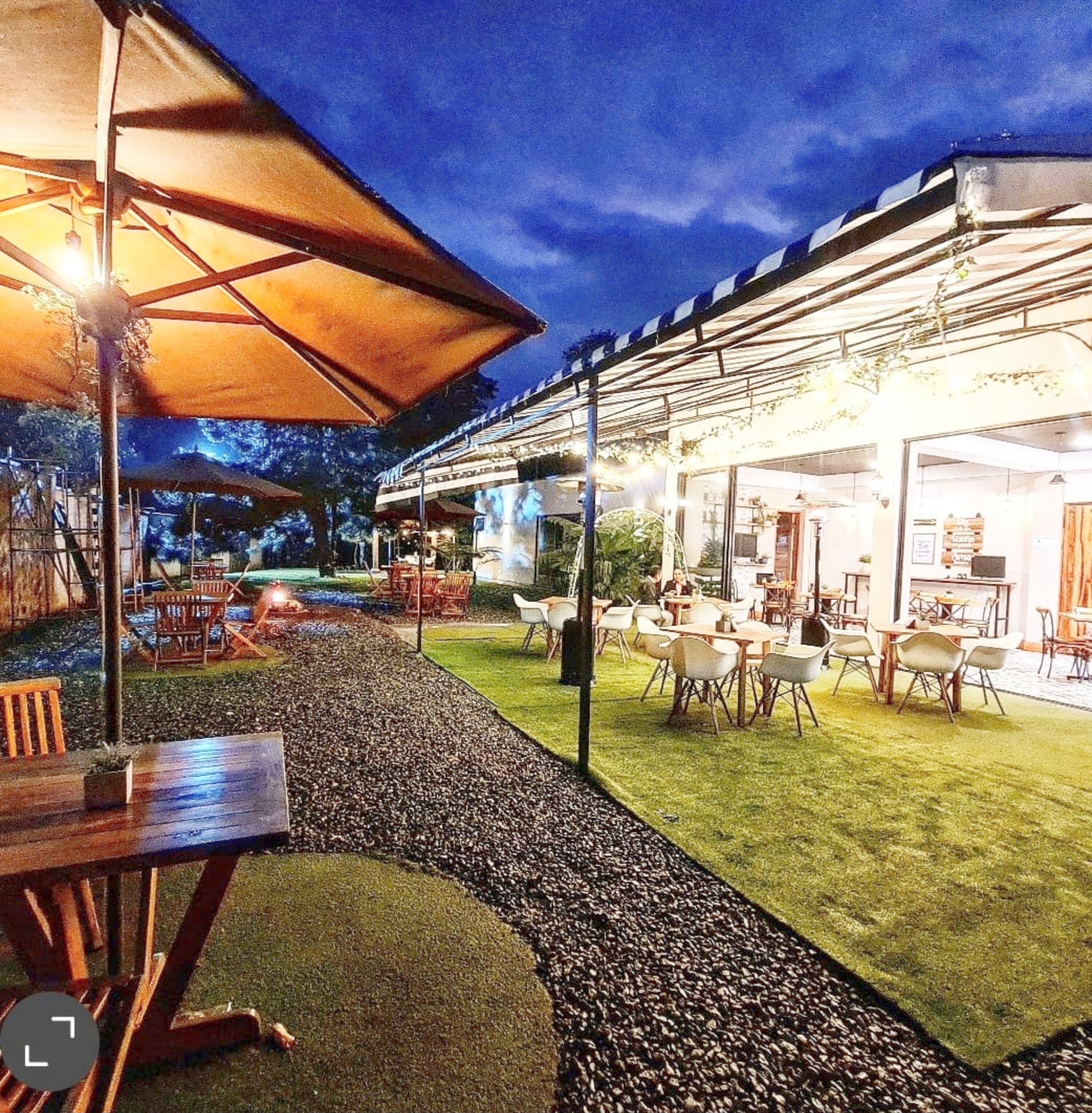 An outdoor dining area with tables and chairs, a covered seating area, and a pool in the background.