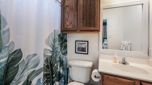 Un baño con inodoro, lavamanos, espejo y cortina de ducha con estampado de hojas.