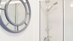 Une salle de bain avec un miroir rond, une douche équipée d’un pommeau de douche à main et un robinet fixé au mur.