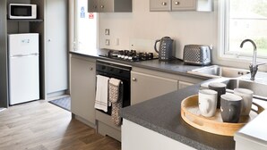 Une cuisine moderne avec des meubles gris, un four encastré, un four à micro-ondes, une bouilloire et un grille-pain.
