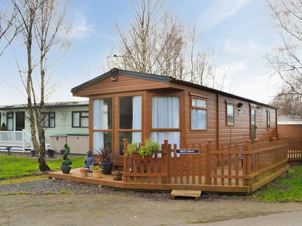 Ein Holz-Mobilheim mit umzäunter Terrasse, einem kleinen Gartenbereich mit Blumentöpfen und einem Schild, das einen Mietpreis angibt.