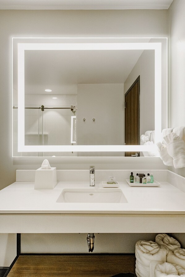 Un baño moderno con un lavamanos blanco, un espejo grande con iluminación LED y un perchero para toallas.