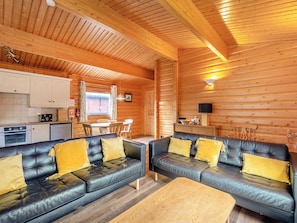 Ein rustikales Holzhaus-Interieur mit Küche, Essbereich und zwei Ledersofas mit gelben Kissen.