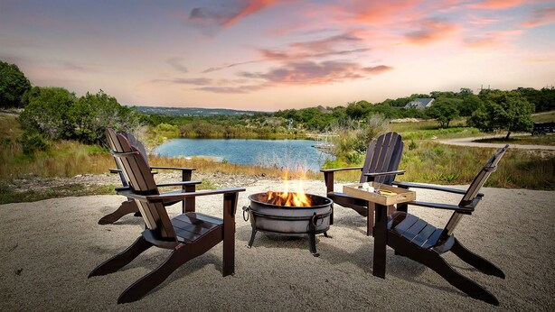 Deux fauteuils Adirondack sont placés face à un feu de camp, avec un lac et des arbres en arrière-plan.