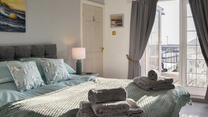 Un dormitorio con cama, almohadas, lámpara, puerta y ventana con cortinas.