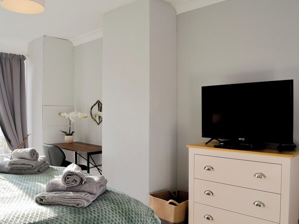 A neatly made bed with folded towels, a television on a wooden cabinet, a desk with a chair, and a mirror on the wall. - 2 bedroom accommodation in Sewerby (Sewerby)
