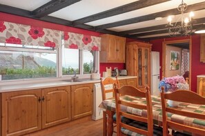 Enjoy meals in this kitchen with an oven and refrigerator, surrounded by a dining table and floral curtains.