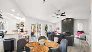 Una sala de estar moderna con una mesa de comedor de vidrio, sofás oscuros y una cocina con barra.