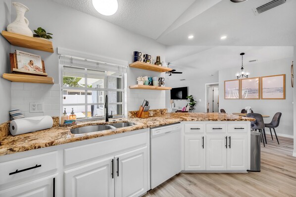 A modern kitchen with white cabinets, a granite countertop, and a built-in dishwasher.