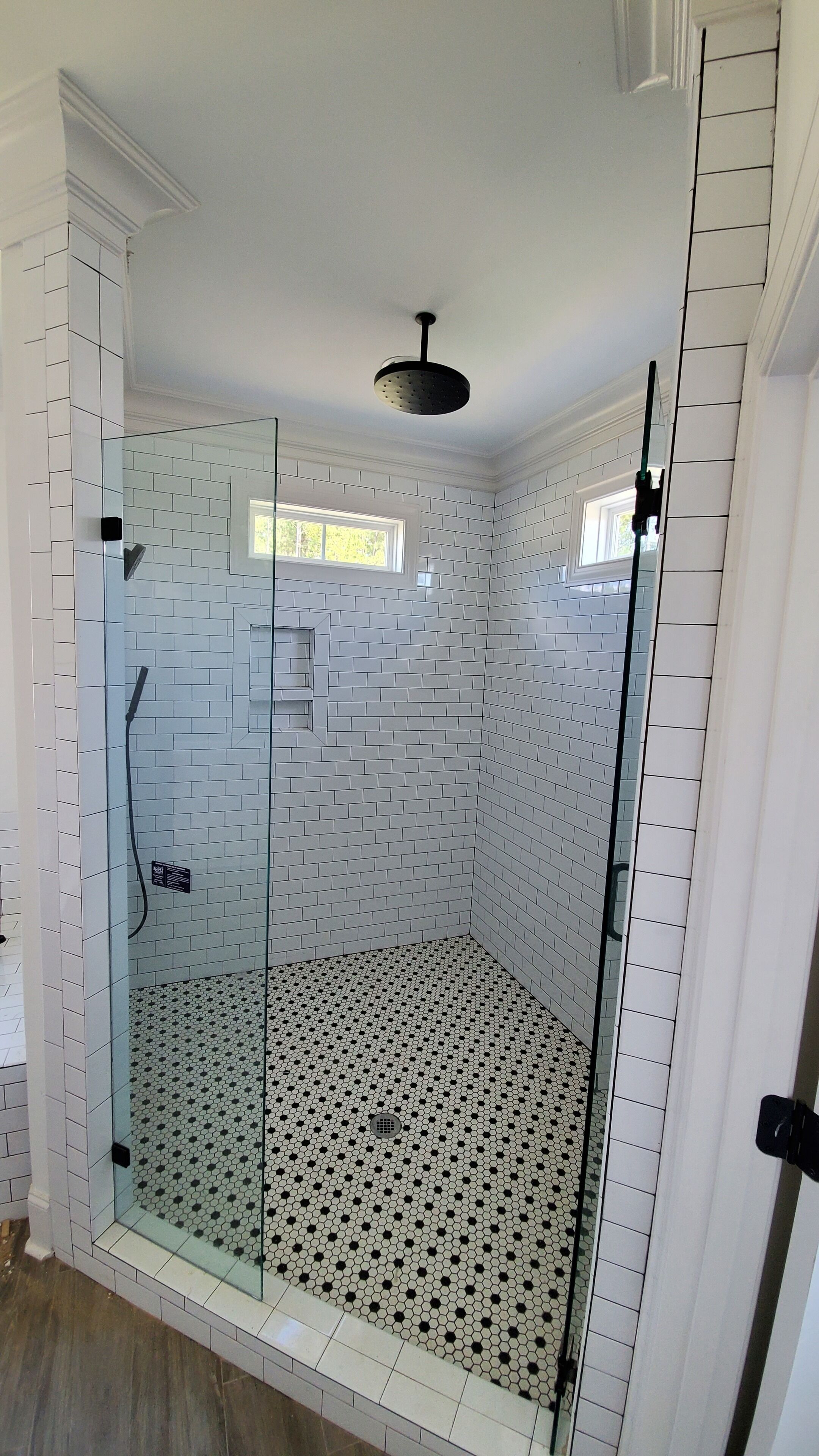 A walk-in shower with white subway tiles and a black and white hexagonal tile floor.