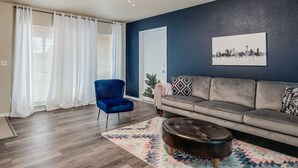 Ein Wohnzimmer mit blauem Sessel, grauem Sofa, Teppich mit Muster und Deckenventilator.