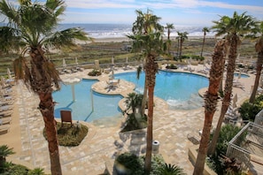 A pool area with palm trees and a view of the beach. - Palisade Palms, Cheerful, Modern Condo with Private Patio and Beachfront Access (Galveston)