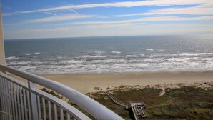 Une vue sur la plage depuis un balcon, avec un ciel dégagé et des vagues sur l’océan.