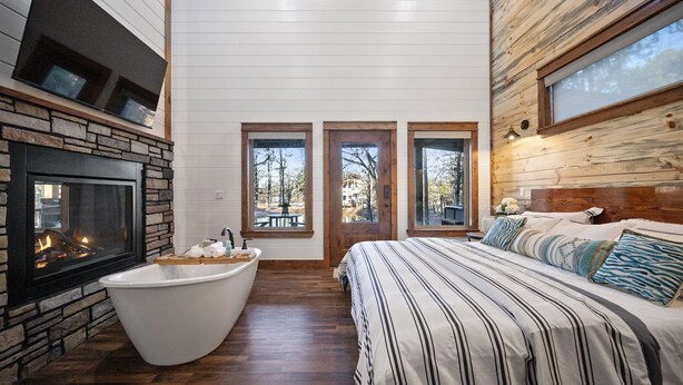 Ein Schlafzimmer mit Kamin aus Stein, einem großen Bett, einer Badewanne und drei Fenstern.