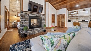 Ein gemütliches Wohnzimmer mit Kamin aus Stein, Holzboden und einer Couch mit floralen Kissen.
