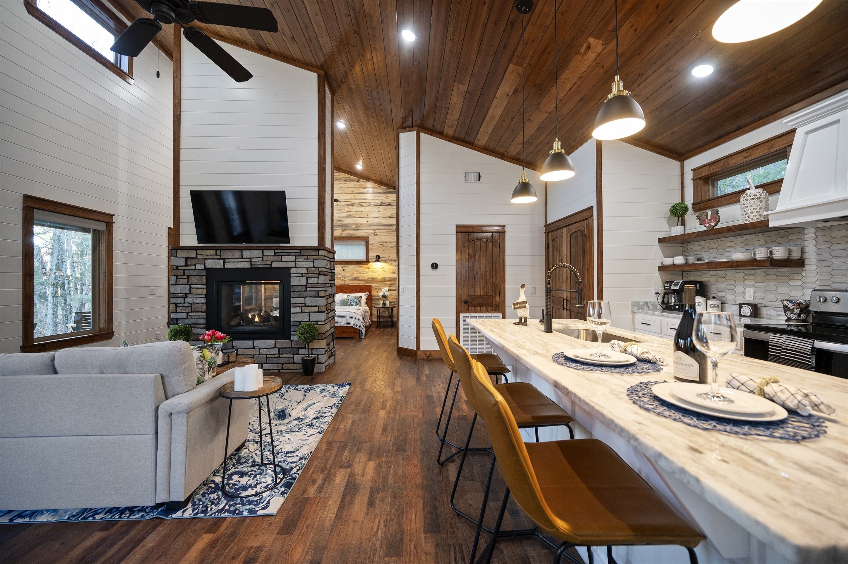 Une cuisine moderne avec une cheminée en pierre, un plafond en bois et un coin repas agrémenté de tabourets de bar.